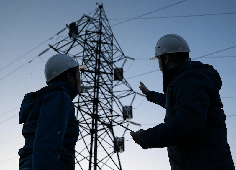 Two tradespeople near an electric power line. 