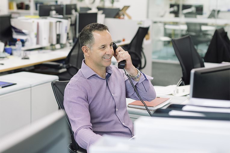 A photograph of a person talking on the phone at a desk in an office. 