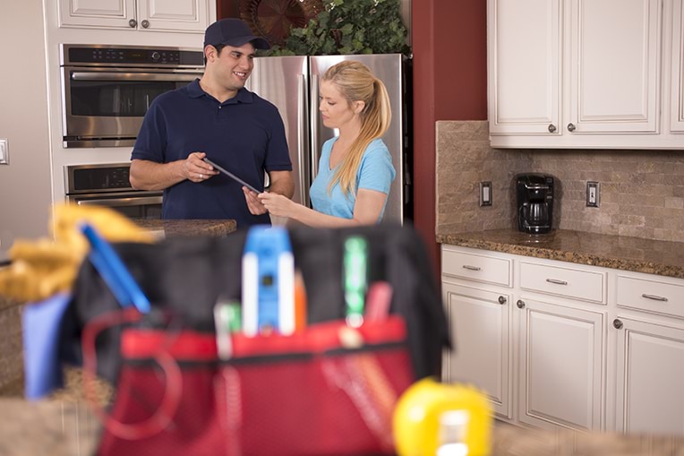 A photograph of a tradesperson talking to a person in their kitchen.