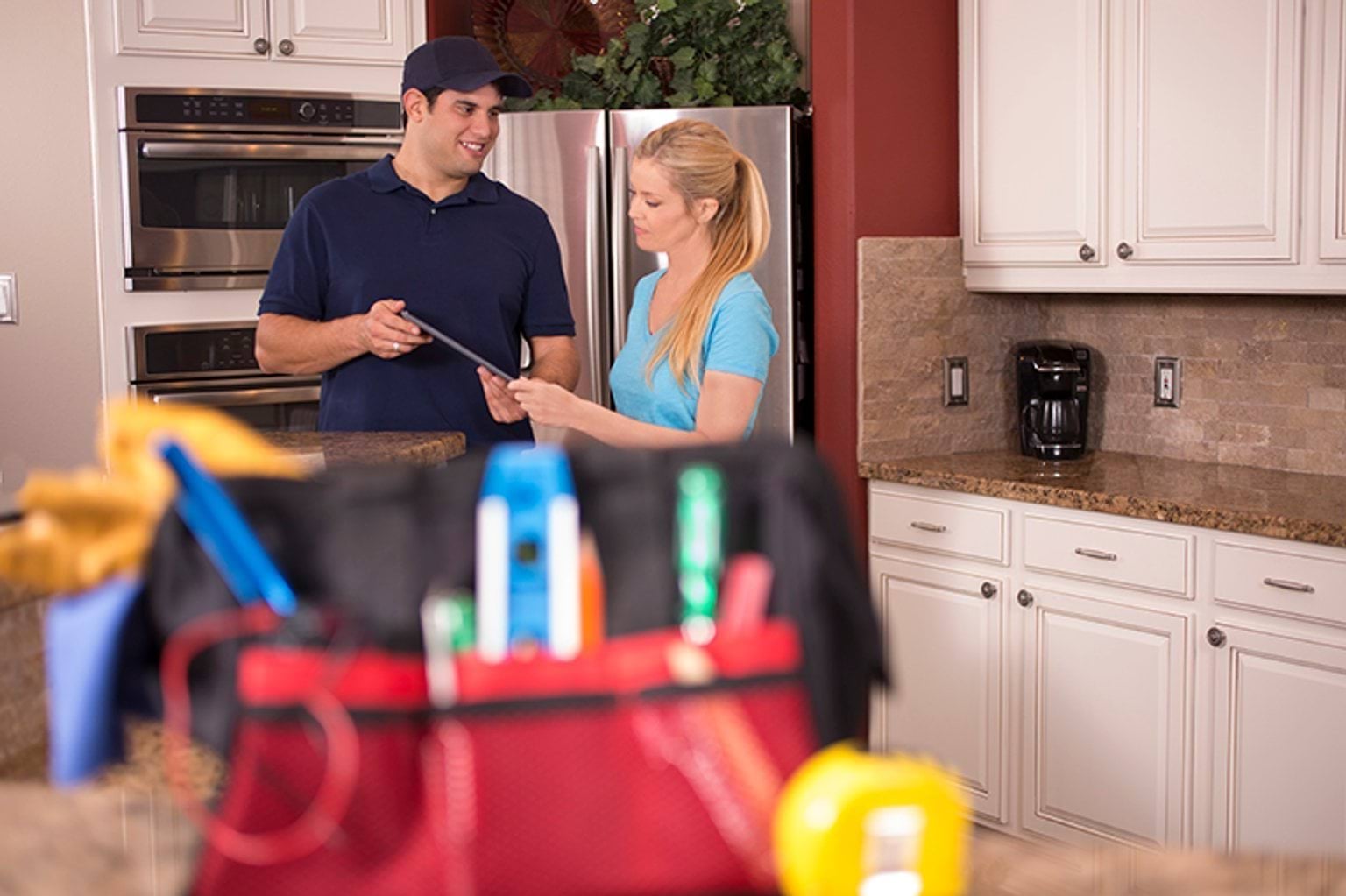 A photograph of a tradesperson talking to a person in their kitchen.