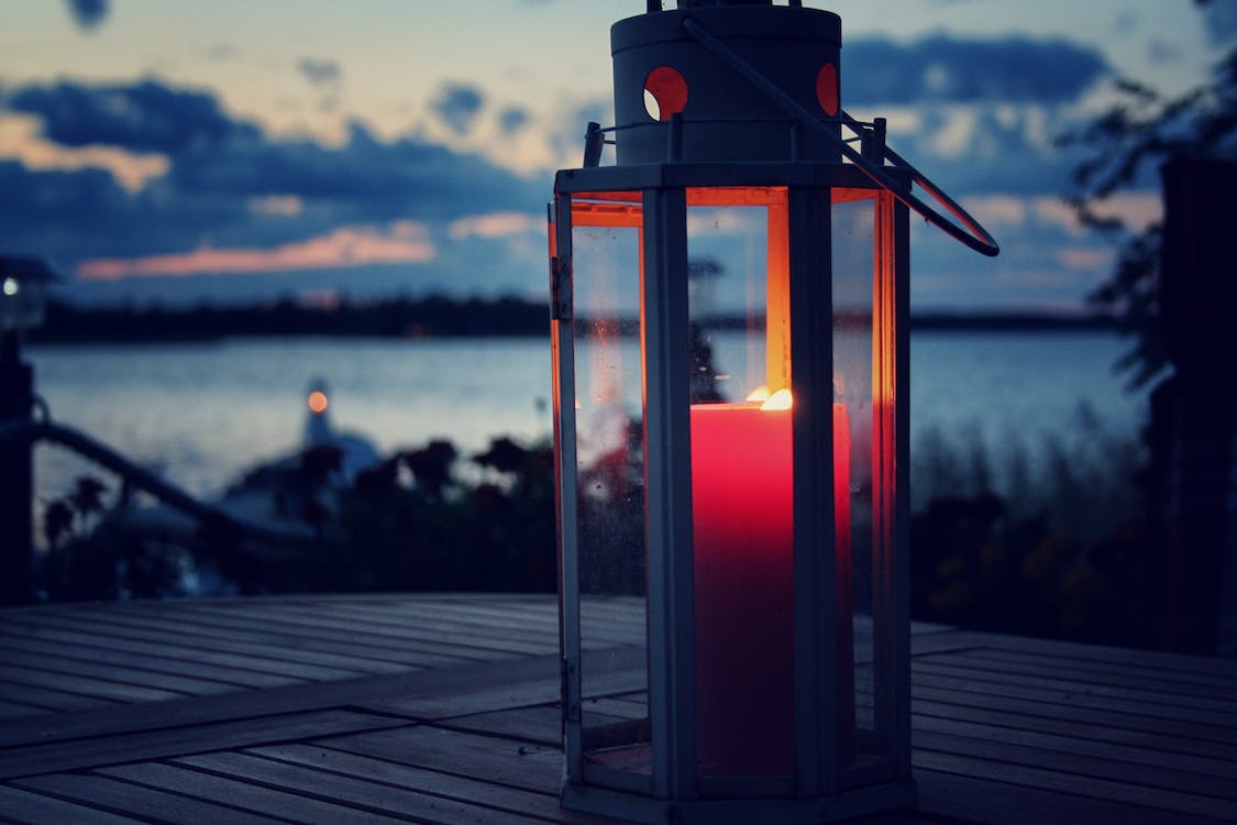 A photograph of a candle-lit lantern on a table near a beach.