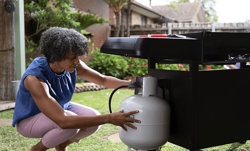 A person checks their liquid petroleum gas canister that's attached to their barbecue in an outdoor setting.