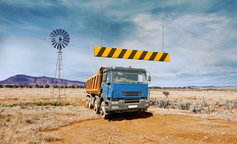 A truck stopped under a hanging bar with 'hazard stripe' pattern – alternating diagonal yellow and black lines – in an wide open rural space. 