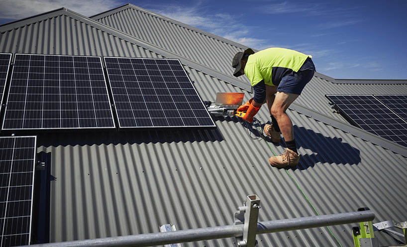 An electrician inspects and works on a solar panel on a roof.